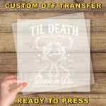 The image is a promotional poster for a custom DTF transfer service. It features a skeleton design with the text "Til Death Do Us Party" and "Amelia's Bachelorette Las Vegas, NV" printed on it. The poster is placed on a wooden surface, and there is a hand holding it up, suggesting that the viewer is ready to press the transfer button.