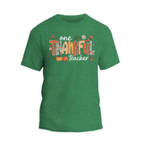 A green t-shirt with a colorful graphic design that says "One Thankful Teacher" in a stylized font.