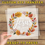 a hand holding a transparent sheet with a wreath design and text on it, placed on a wooden surface.