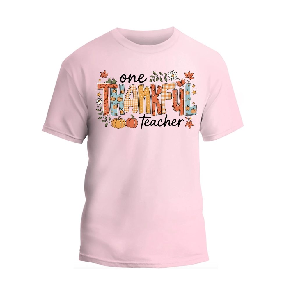 A pink t-shirt with a graphic design featuring the text "One Thankful Teacher" surrounded by autumn-themed elements such as leaves, pumpkins, and flowers.