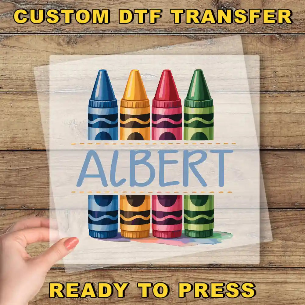 a hand holding a transparent sheet with a colorful illustration of crayons on it, along with the word "ALBERT" written below the crayons.