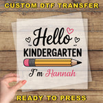 A hand holding a piece of paper with a hand-drawn pencil and the text "Hello Kindergarten I'm Hannah" printed on it.