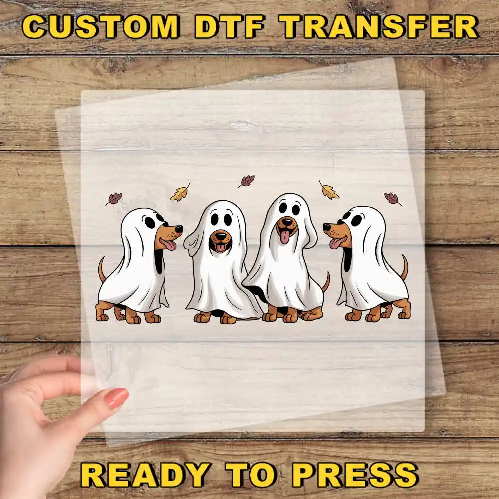 A hand is holding a transparent sheet with a cartoon image of four ghostly dogs in a Halloween-themed illustration.