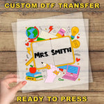 A hand holding a transparent sheet with a colorful illustration of various school-related objects, including a globe, books, a pencil, and a laptop, along with the text "Mrs. Smith" and "READ ME" printed on it.