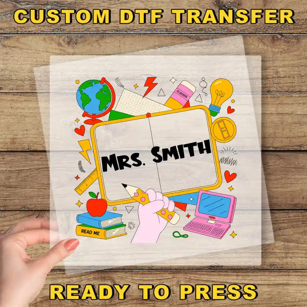 A hand holding a transparent sheet with a colorful illustration of various school-related objects, including a globe, books, a pencil, and a laptop, along with the text "Mrs. Smith" and "READ ME" printed on it.