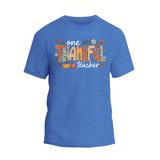 A blue t-shirt with a graphic design featuring the text "One Thankful Teacher" surrounded by various fall-themed elements such as pumpkins, leaves, and flowers.