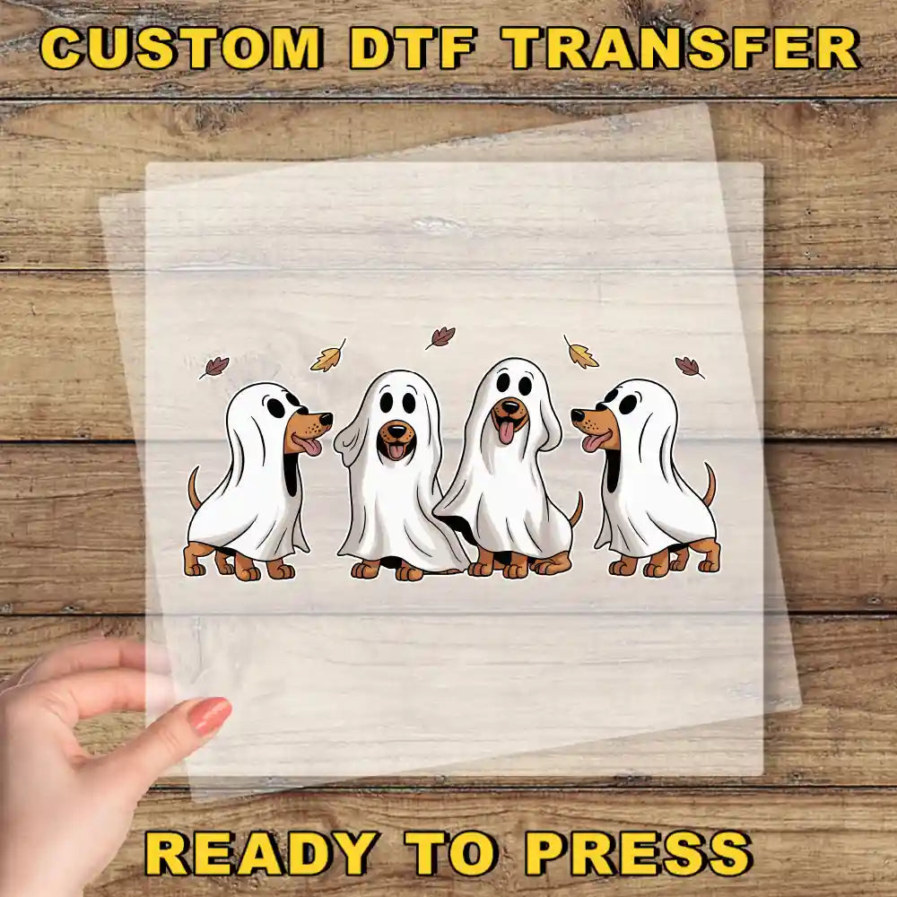 A hand is holding a transparent sheet with a cartoon image of four dogs dressed as ghostly figures, with leaves floating around them.
