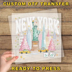 A hand is holding a transparent sheet with a colorful illustration of New York City, including the Statue of Liberty, Christmas trees, and taxis.