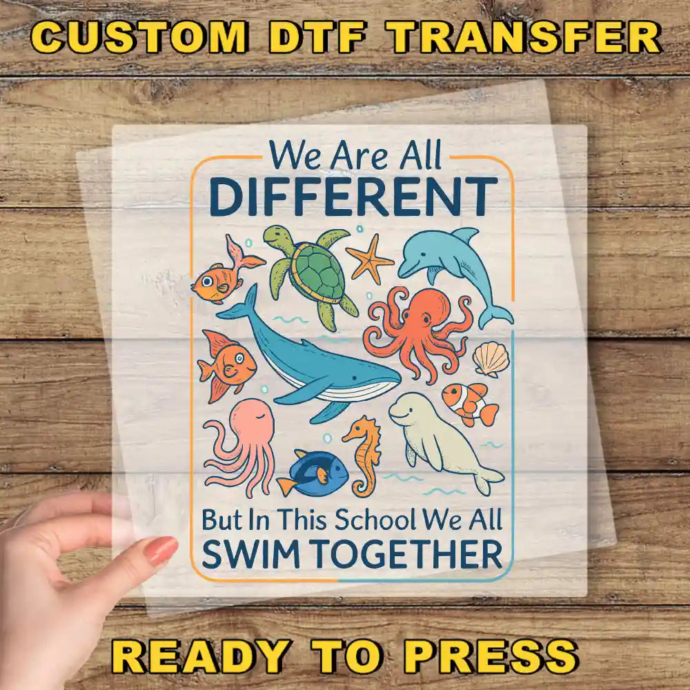 The image is a hand holding a clear sheet with a colorful illustration of various sea animals, including a whale, octopus, and starfish, along with the text "We Are All Different But in This School We All Swim Together".