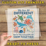 The image is a hand holding a clear sheet with a colorful illustration of various sea animals, including a whale, octopus, and starfish, along with the text "We Are All Different But in This School We All Swim Together".