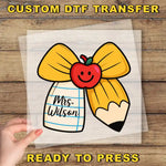 A hand is holding a clear sheet with a cartoon image of a pencil and a smiley face, along with the text "Mrs. Wilson" written on it.