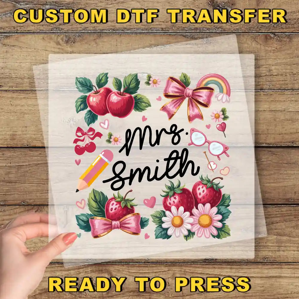 The image is a hand holding a transparent sheet with a colorful illustration of various objects, including apples, flowers, and a pencil, along with the text "Mrs. Smith" and "Ready to Press".