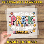The image is a hand holding a piece of paper with a colorful and playful design featuring the text "Watch out PRE-K here I come!" and various decorative elements such as flowers, lightning bolts, and a pencil.