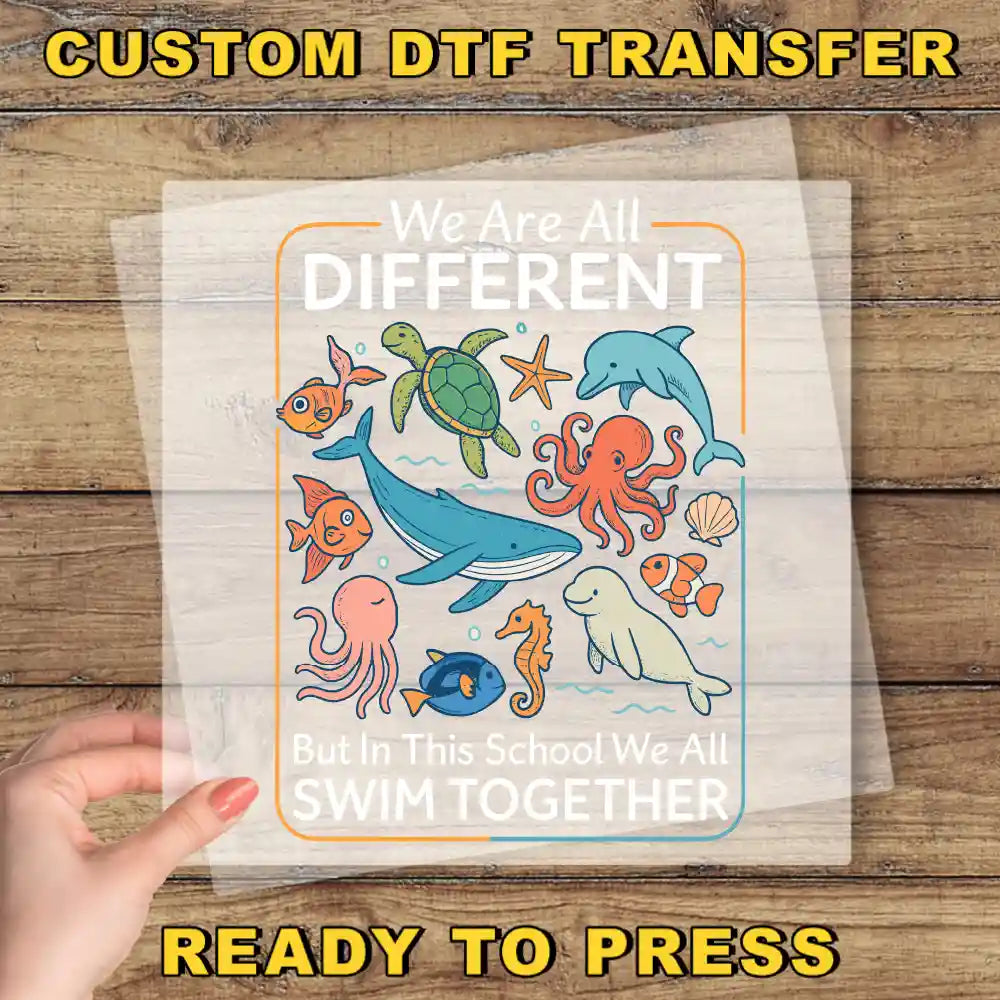 The image is a hand holding a clear sheet with a colorful illustration of various sea animals, including a whale, octopus, and dolphin, along with the text "We Are All Different But in this School We All Swim Together".
