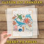 The image is a hand holding a clear sheet with a colorful illustration of various sea animals, including a whale, octopus, and dolphin, along with the text "We Are All Different But in this School We All Swim Together".