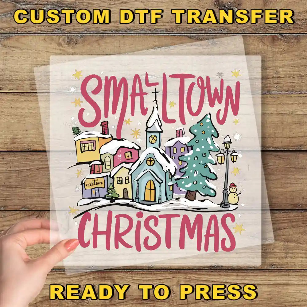 The image is a hand holding a transparent sheet with a colorful illustration of a small town during Christmas, featuring a church, houses, trees, and snow.