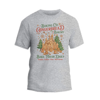 A gray t-shirt with a graphic design featuring a gingerbread house and the text "Baking Co. Gingerbread Bakery Bake Fresh Daily Cookies Cakes Pies Hot Cocoa".