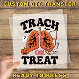 The image is a Halloween-themed graphic with a hand holding a clear sheet of the design. The design features a Halloween-themed lung with the text "TRACK OR TREAT" and various Halloween-related elements such as a ghost, a pumpkin, and a stethoscope.